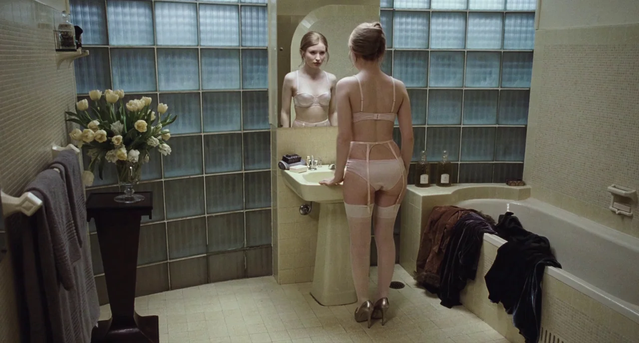 Sleeping Beauty (2011) movie still: fullbody — A tiled bathroom features glass block walls, a pedestal sink, and a bathtub. A young woman in…