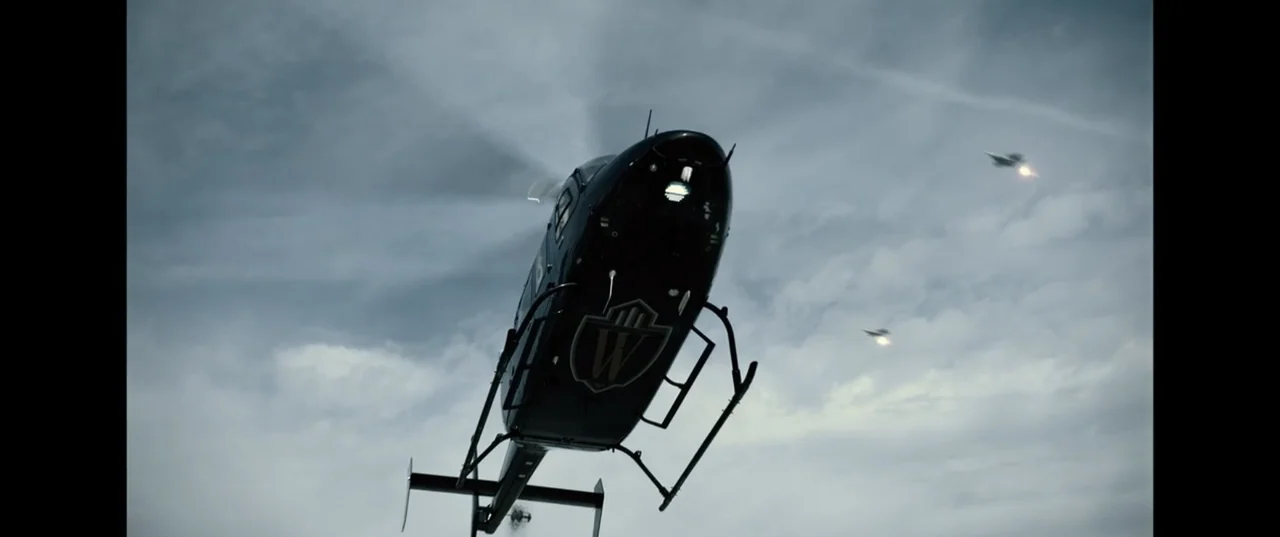 Batman v Superman: Dawn of Justice (2016) movie still: fullbody — A dark-colored corporate helicopter flies across a cloudy, grey daytime sky. Two…