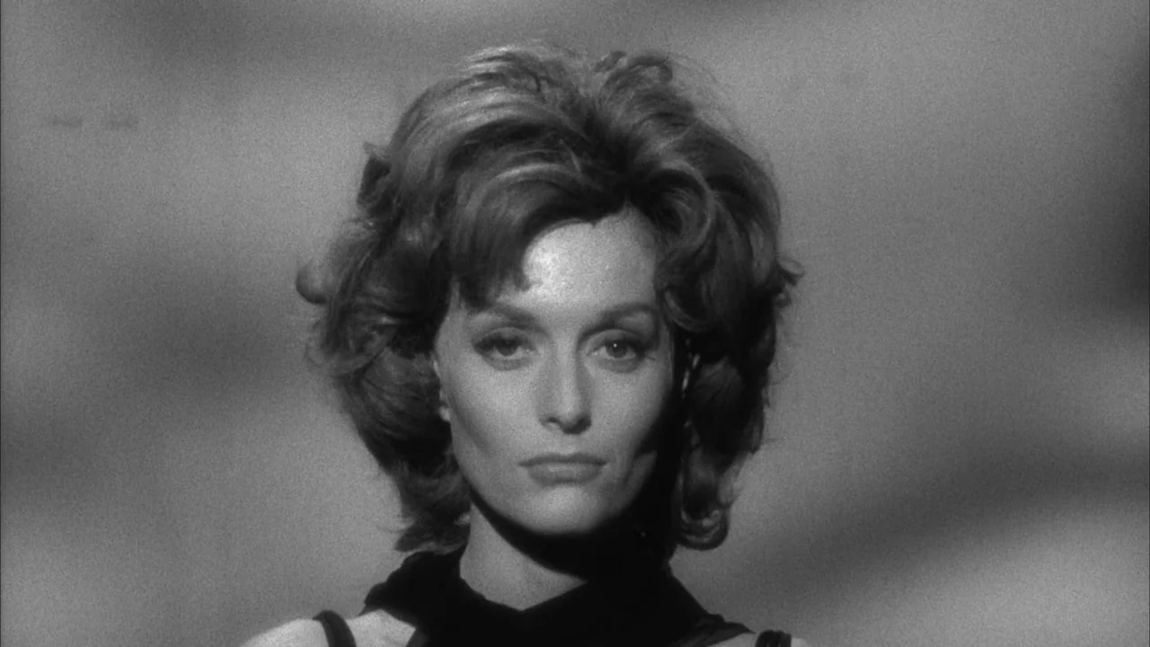 The Naked Kiss (1964) movie still: closeup — A head-and-shoulders portrait of a woman against a textured grey background. She gazes directly into…