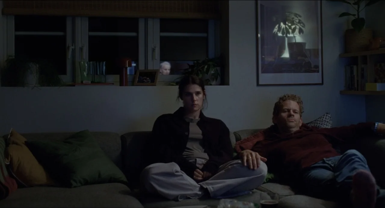 Sentimental Value (2025) movie still: medium — A modern living room at night with a large window in the background. A man and a woman sit side by…