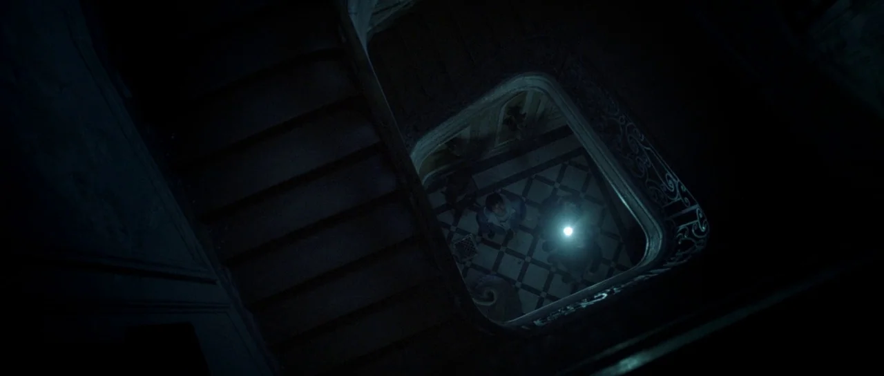Livid (2011) movie still: wide — An ornate interior stairwell viewed from the top floor looking down at the ground. Two individuals stand at the…