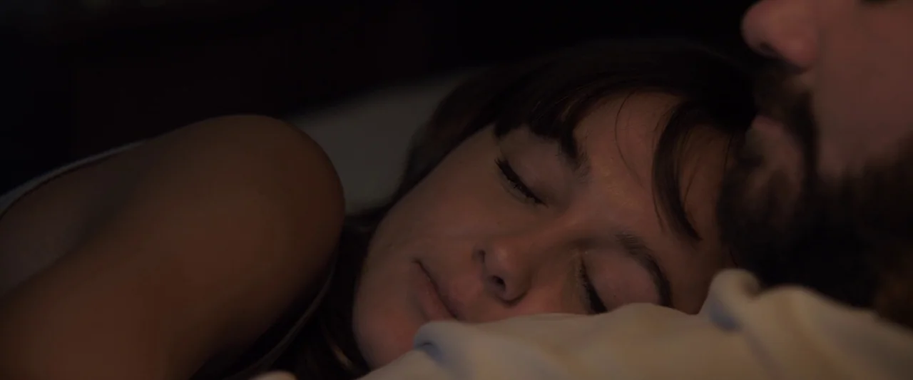 You’re Next (2013) movie still: closeup — Two people lie close together in a dark room during the night. A woman sleeps with her head on a pillow…