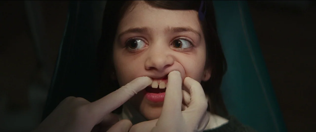 Humanist Vampire Seeking Consenting Suicidal Person (2023) movie still: closeup — A young child sits in a dental chair during an examination. Hands…