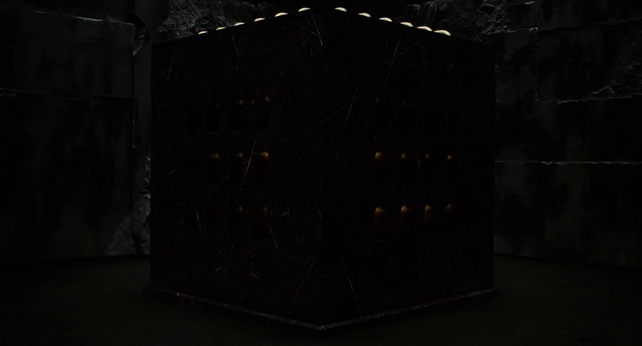 The Immortals (2011) movie still: wide — A dark stone room contains a large black marble cube with gold detail. The cube has grid-like indentations…