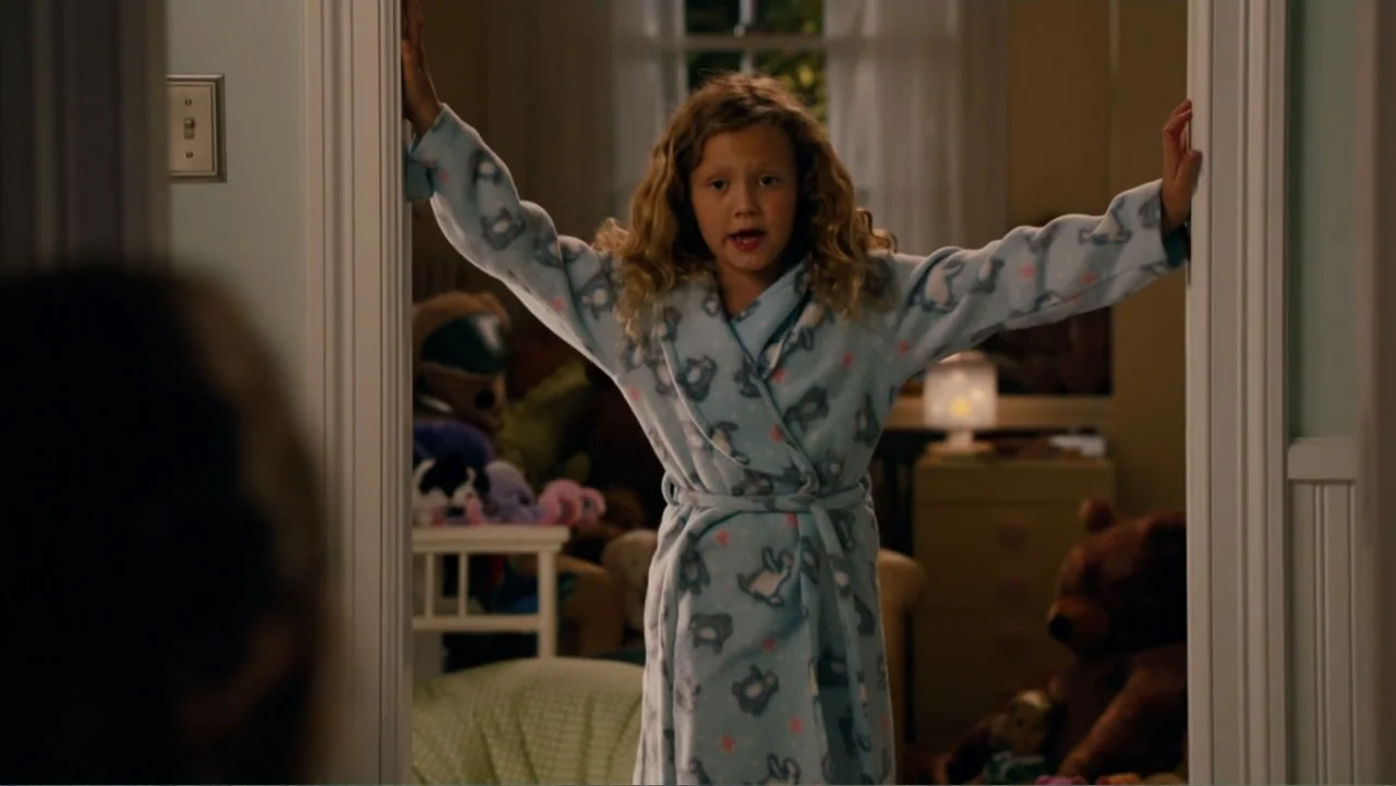 This Is 40 (2012) movie still: medium — A child stands in a bedroom doorway frame with stuffed toys visible in the background. The girl is…