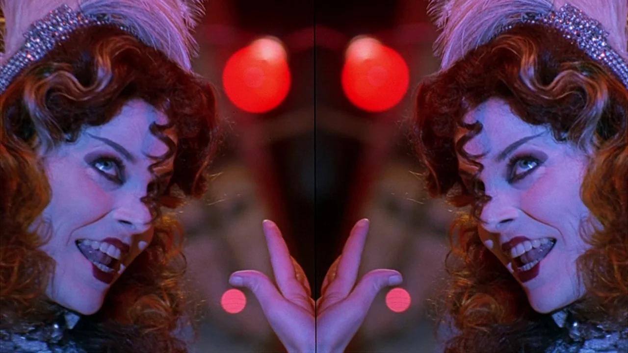 House of 1000 Corpses (2003) movie still: closeup — A theatrical performer with heavy stage makeup poses under vivid red and blue lights. The…
