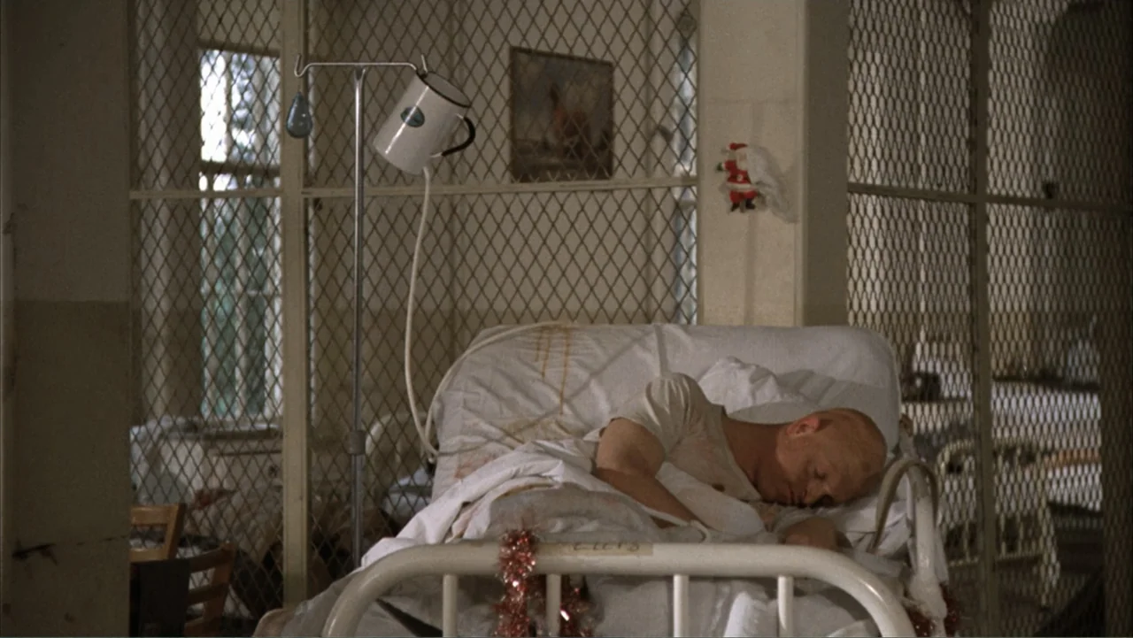 One Flew Over the Cuckoo's Nest (1975) movie still: medium — A sterile ward room features metal cage partitions and a single hospital bed. A bald…