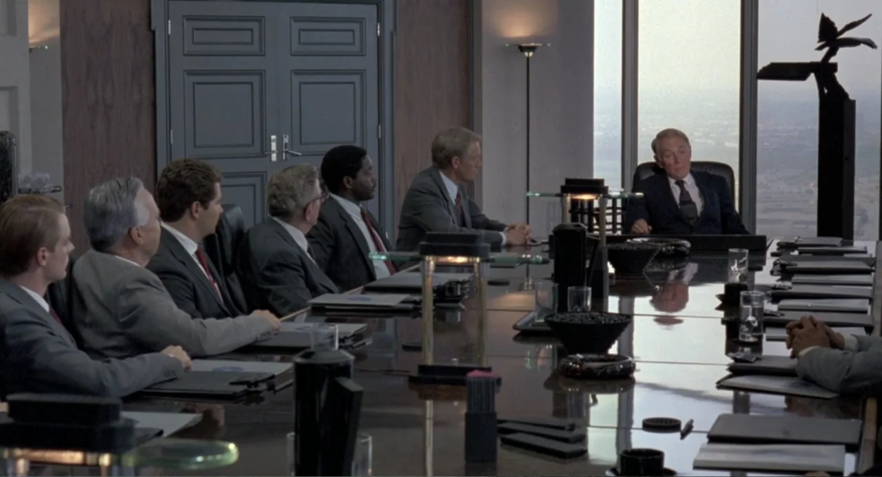 RoboCop (2014) movie still: wide — A high-rise executive conference room features a long dark table and large windows. Seven men in suits sit around…
