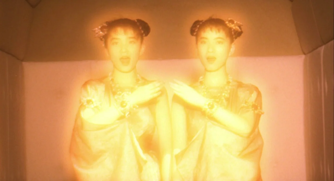 Godzilla and Mothra: The Battle for Earth (1992) movie still: medium — Two identical women stand side-by-side within a padded, light-colored…