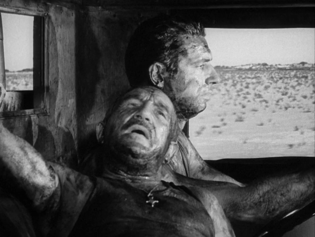 The Wages of Fear (1953) movie still: medium — The interior of a truck cab reveals two grimy men driving through a desert. One man leans back while…