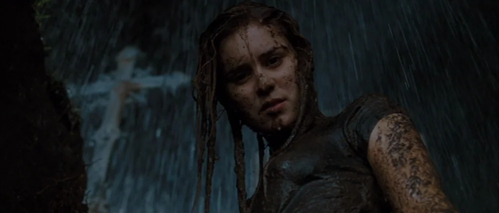 Drag Me to Hell (2009) movie still: medium — A nighttime cemetery setting with heavy rain falling in the darkness. A young woman covered in mud…