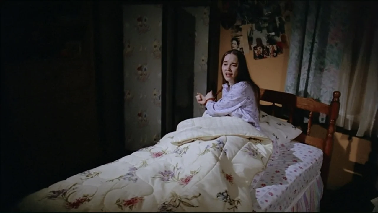 O código oculto (2025) movie still: medium — A dimly lit room features a bed with floral bedding and walls covered in posters. A young woman with…
