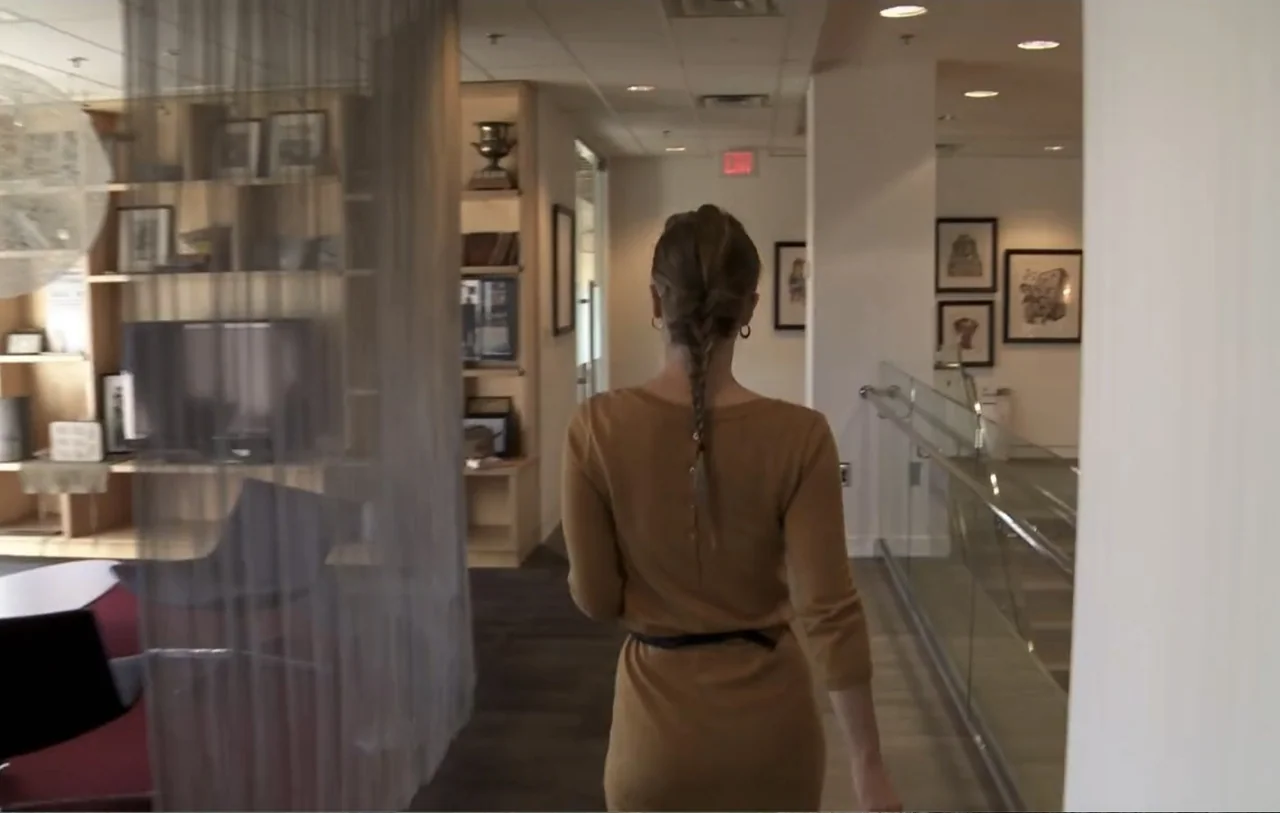 No Place to Hide (1992) movie still: fullbody — A modern office space features wooden shelving units and framed artwork on white walls. A woman with…