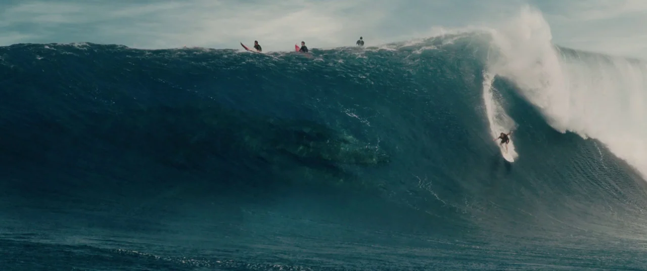 Jurassic World: Fallen Kingdom (2018) movie still: wide — A massive deep blue breaking ocean wave rises over a wide expanse of water. A surfer…