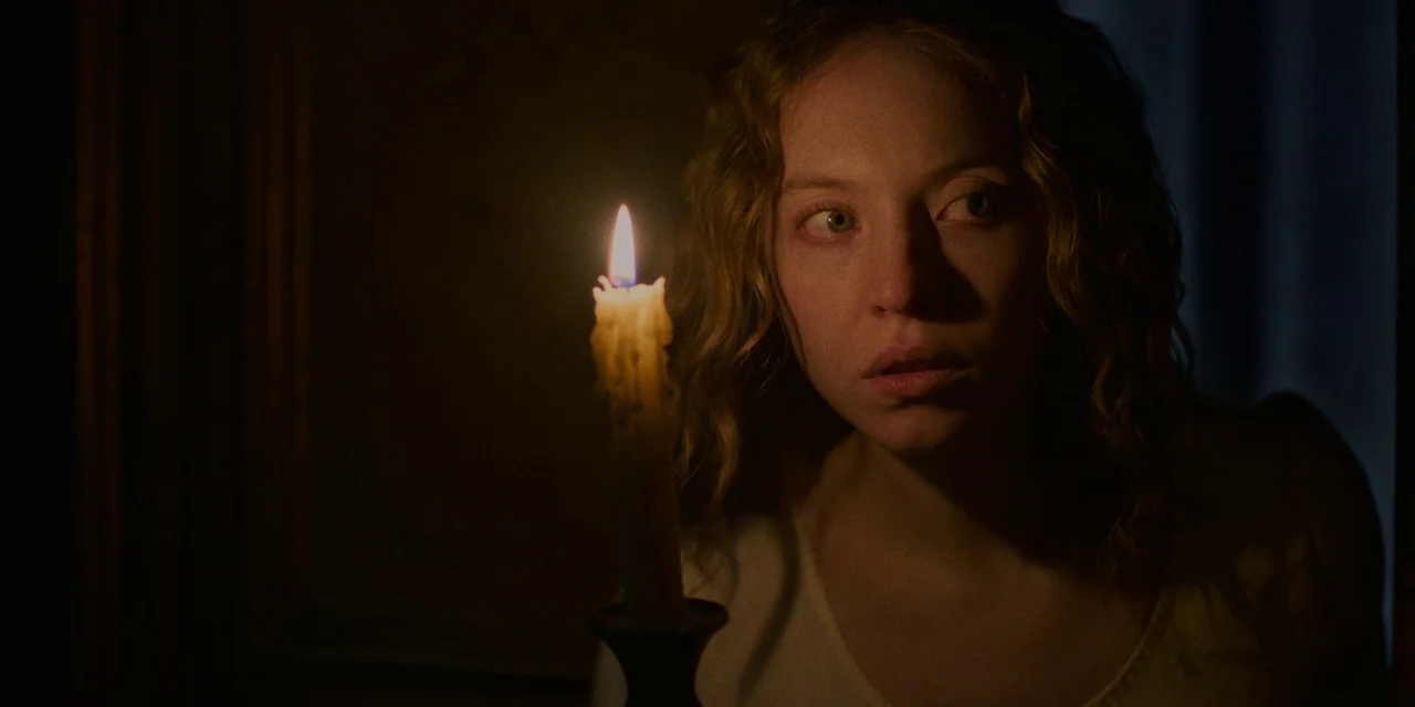 Immaculate (2024) movie still: closeup — A dimly lit room is shrouded in darkness, with only the immediate area illuminated. A woman stares past the…