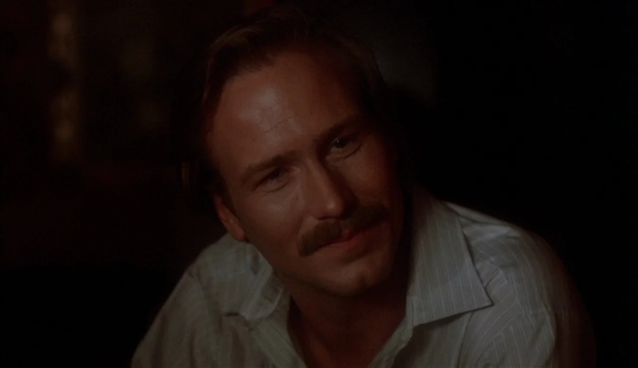 Body Heat (1981) movie still: closeup — A dark indoor setting features a man in shadows. He looks toward the side while wearing a white shirt.