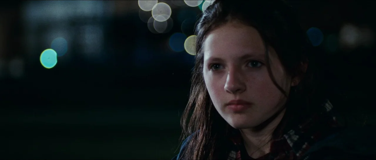 Election (1999) movie still: closeup — A night scene featuring a young woman standing outdoors in an urban environment. Blurred spherical lights…