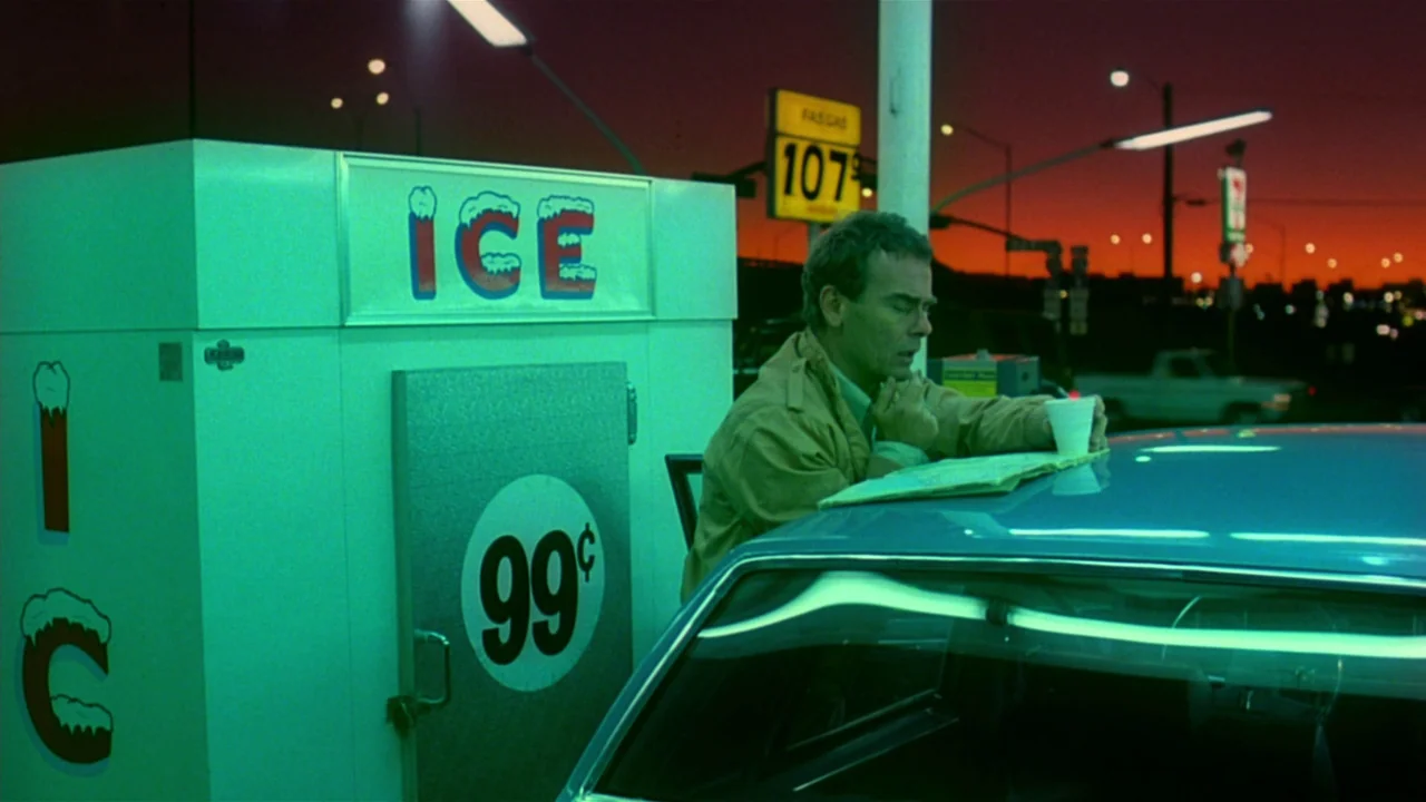 Paris, Texas (1984) movie still: medium — A man stands by a car at a gas station under artificial green lighting. He looks at a map spread out on…