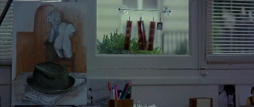 The Truth About Charlie (2002) movie still: medium — A workspace features a painting of a nude statue and a fedora hat. Film strips hang from…