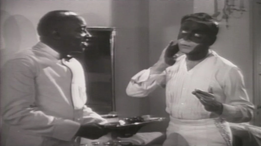 Bamboozled (2000) movie still: medium — A small dressing room featuring a wall mirror and a vanity surface. One man holds a serving tray while the…