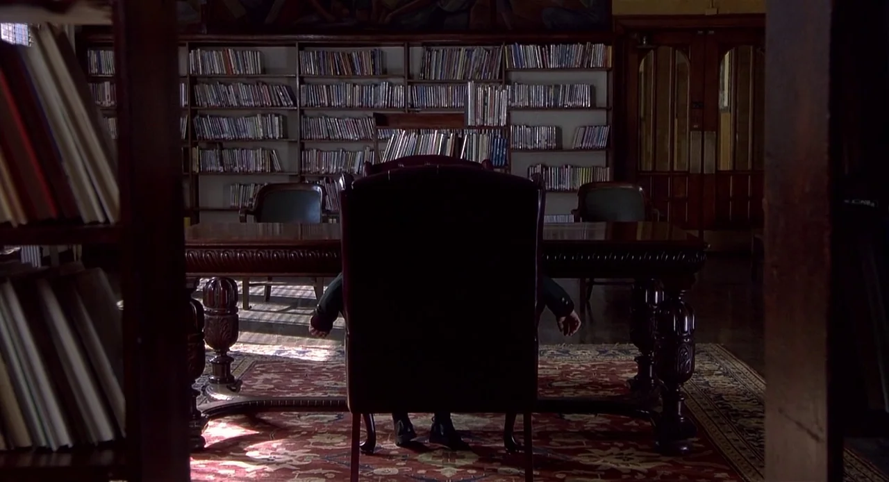 The Sixth Sense (1999) movie still: medium — A dark, wood-paneled room features floor-to-ceiling bookshelves filled with volumes and a patterned…