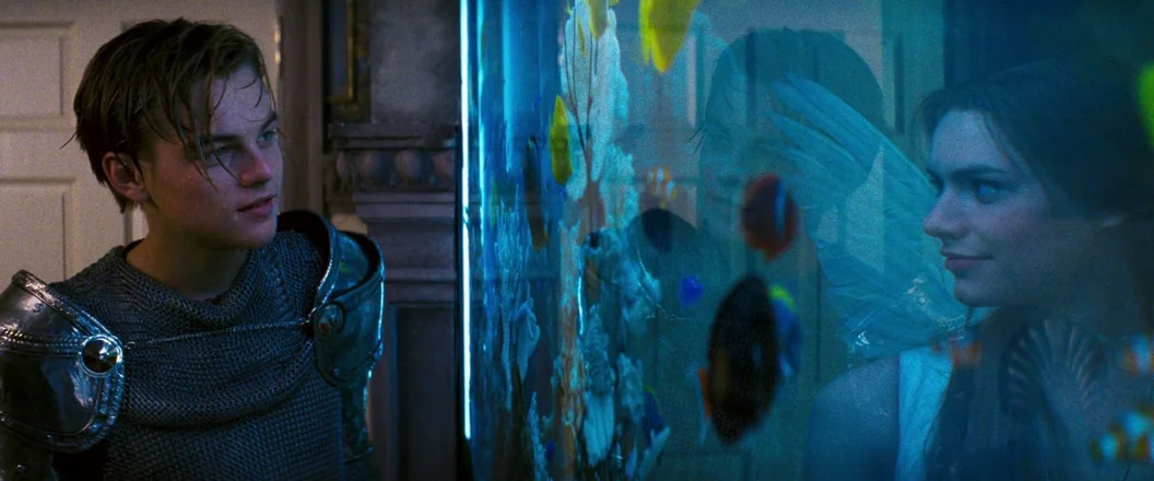 Romeo + Juliet (1996) movie still: medium — An interior space features a large, glowing blue aquarium partition dividing the subjects. A man in…
