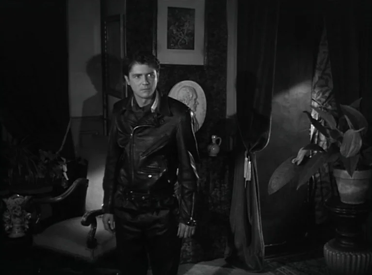 Head Against The Wall (1959) movie still: medium — A dimly lit room contains Victorian decor including framed art and a profile medallion. A man in…