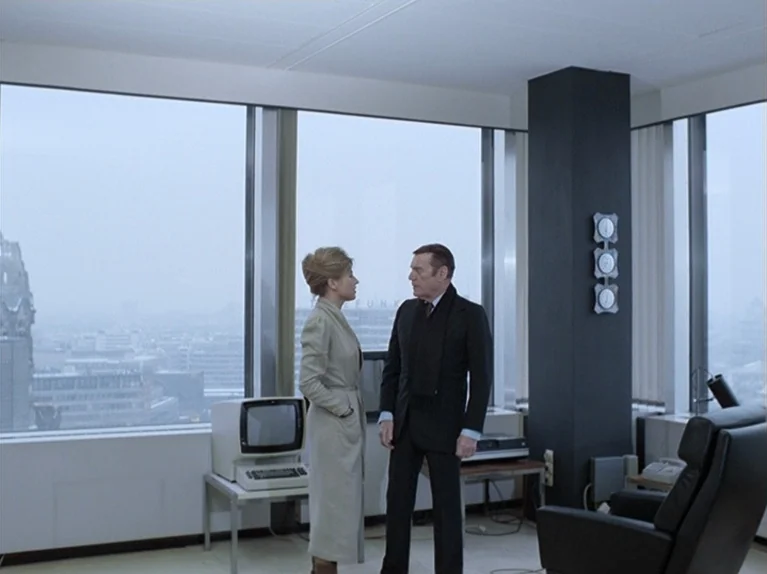 The Third Generation (1979) movie still: fullbody — A sterile, minimalist high-rise workspace features floor-to-ceiling windows overlooking a hazy…