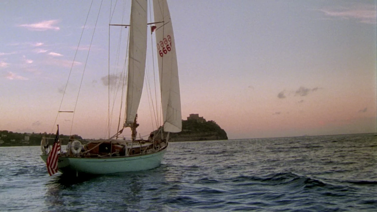 The Talented Mr. Ripley (1999) movie still: wide — A sailboat with white sails floats on the calm ocean during twilight hours. A distant rocky…