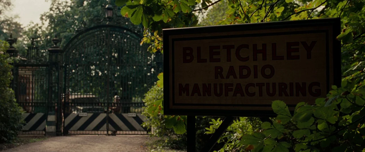 The Imitation Game (2014) movie still: establishing — A wrought-iron gate stands closed at the entrance to a wooded property. A prominent sign in…