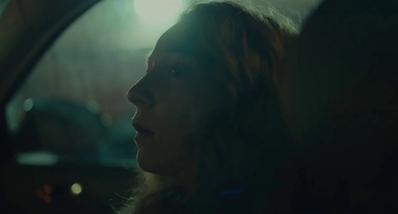 Private Life (2018) movie still: closeup — The interior of a vehicle at night is illuminated by dim external light. A woman sits in the driver seat…