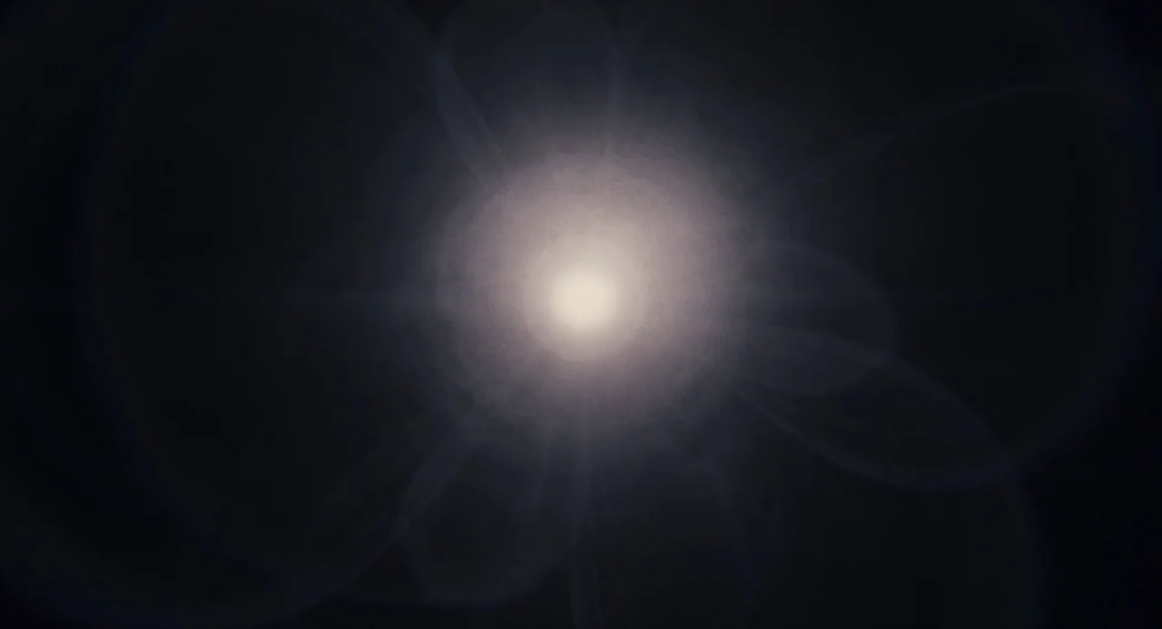 Martyrs (2008) movie still: closeup — A bright central light point glows against an entirely dark black void. Multiple circular lens flares radiate…