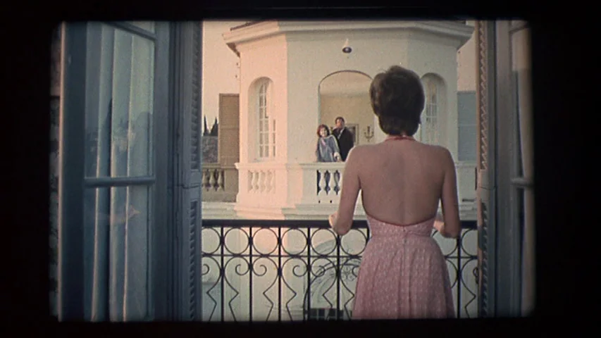 Day for Night (1973) movie still: medium — An outdoor Mediterranean-style terrace features a woman standing at an iron railing. Beyond her, two…