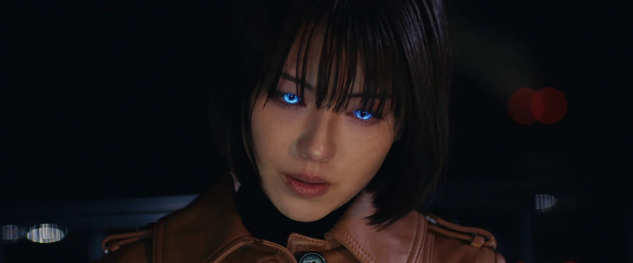 Shin Kamen Rider (2023) movie still: closeup — A dark environment at night with blurred city lights visible in the distant background. A young woman…