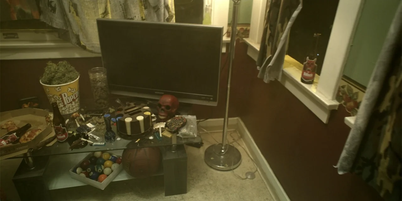 7th & Union (2021) movie still: medium — A cluttered glass coffee table sits in a corner of a living room. Various personal items, snacks, and a…