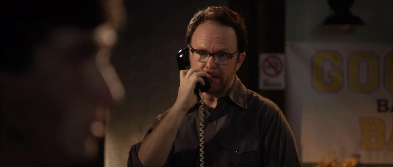 Jeepers Creepers 3 (2017) movie still: medium — A dimly lit indoor space with a man talking on a corded telephone. The man in the middle distance…