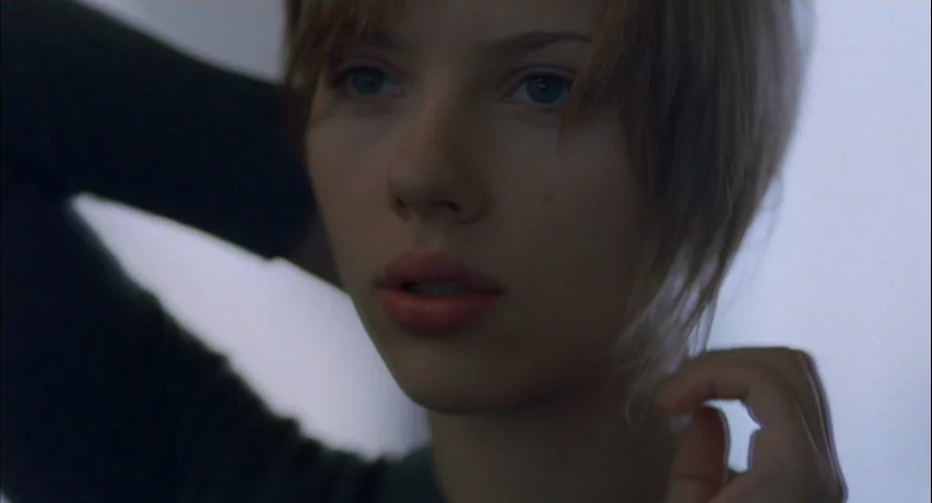 Lost In Translation (2003) movie still: closeup — A close-up of a person inside a room with plain walls. The woman adjusts her hair while looking…