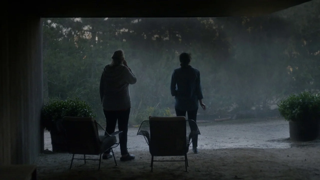Marjorie Prime (2017) movie still: fullbody — A dark, covered patio area opens out toward a dense, rain-filled pine forest. Two women stand…