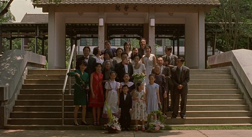 Yi-Yi (A One and A Two) (2000) movie still: wide — A group of people are arranged in rows on wide stone outdoor stairs. They are posing formally for…