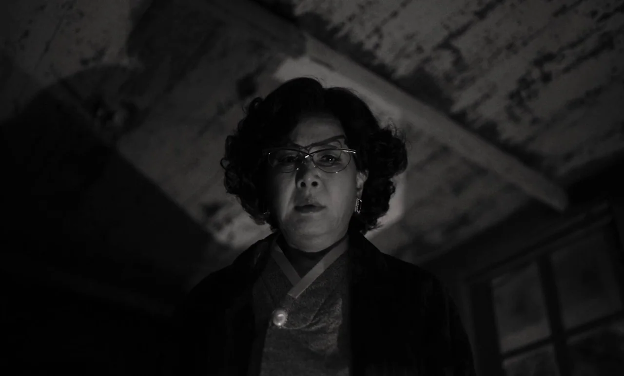 Cobweb (거미집) (2023) movie still: medium — An attic space with exposed wooden beams and dim, textured rafters above. A woman looks down from above as…