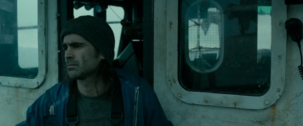 Ondine (2009) movie still: medium — A cramped and weathered cabin interior of a boat with metallic surfaces and windows. A man in a knit cap sits…