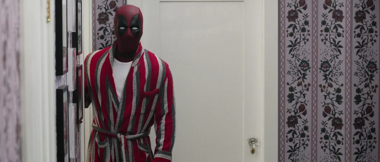 Deadpool (2016) movie still: medium — A narrow residential hallway features patterned floral wallpaper and white-painted doorways. A masked…