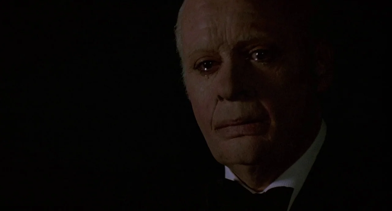 Chaplin (1992) movie still: closeup — An elderly man is framed against a void of deep, impenetrable black. He wears a tuxedo and has tears running…