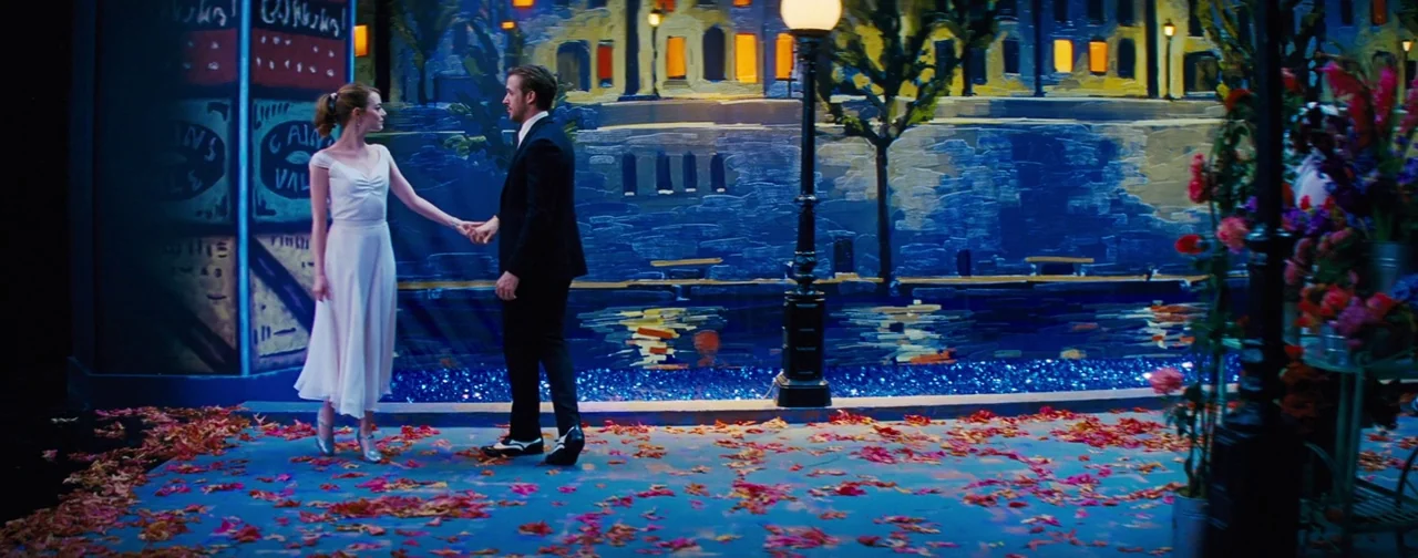 La La Land (2016) movie still: fullbody — A theatrical stage set features a painted backdrop depicting a canal at night. A man and woman stand on a…
