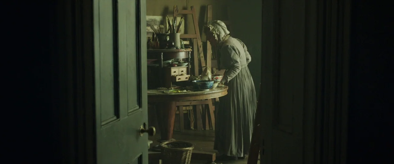 Mr. Turner (2014) movie still: medium — A cluttered nineteenth-century workspace contains easels, brushes, and a heavy wooden round table. An older…