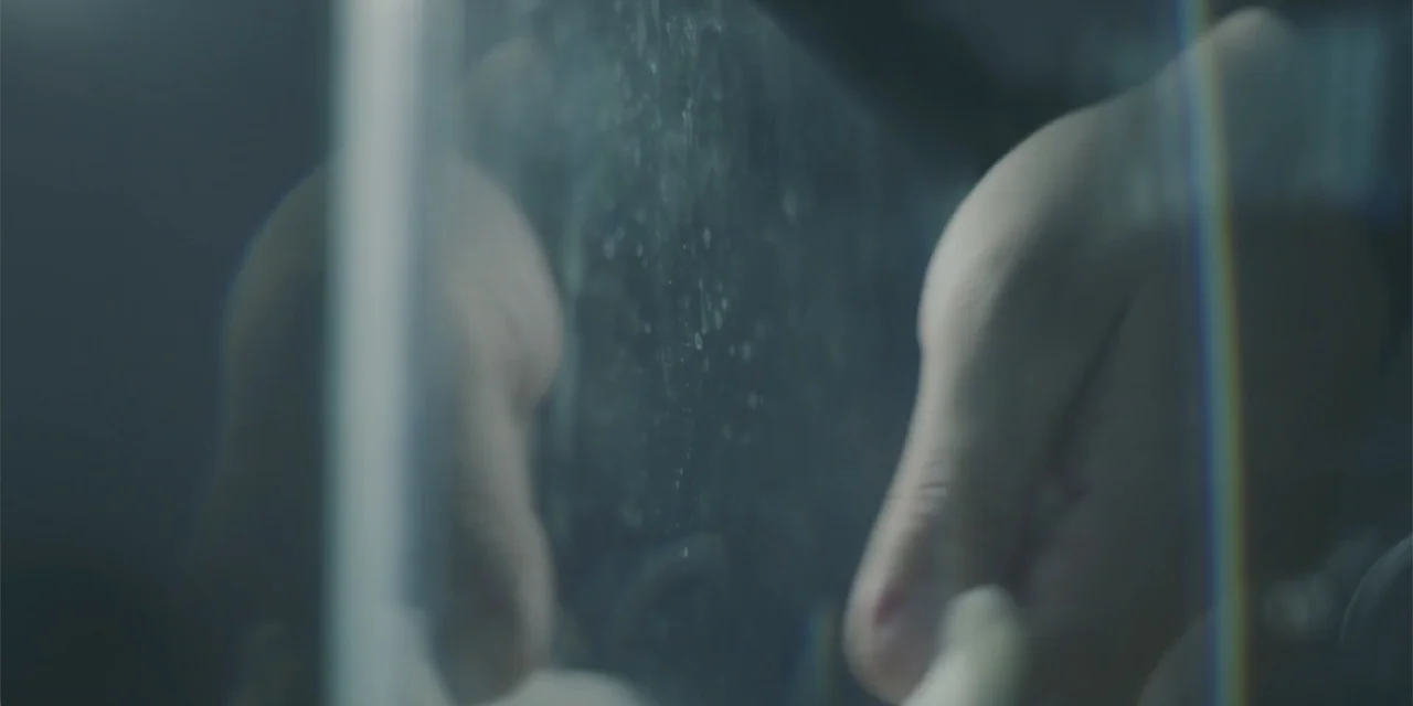 Lobos (2019) movie still: closeup — A close view of two hands pressing against a translucent, dust-covered pane of glass. The scene focuses on the…