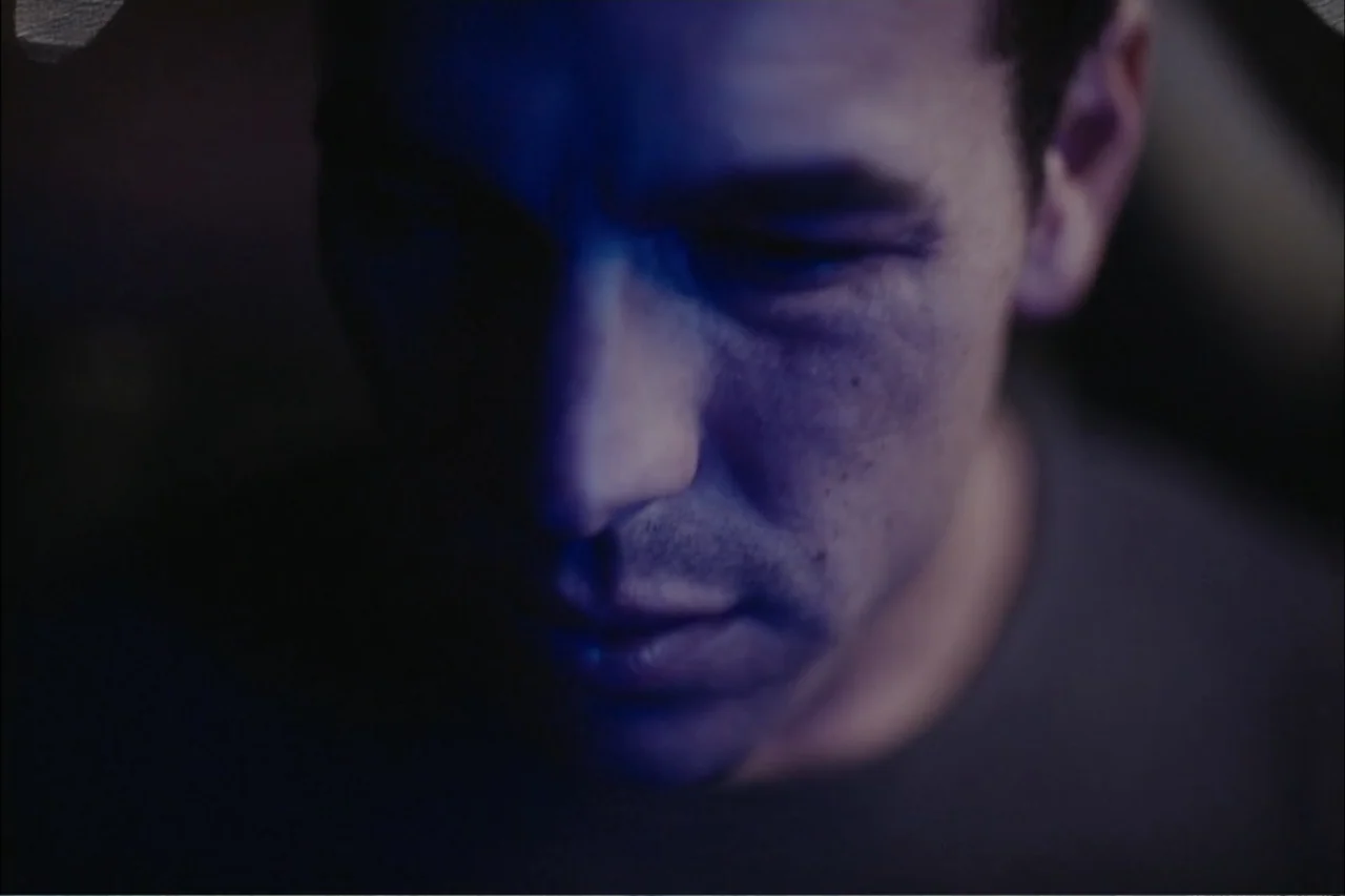 Cross the Line (2020) movie still: closeup — A dark vehicle interior at night features low-level blue light illuminating the driver. A man with…