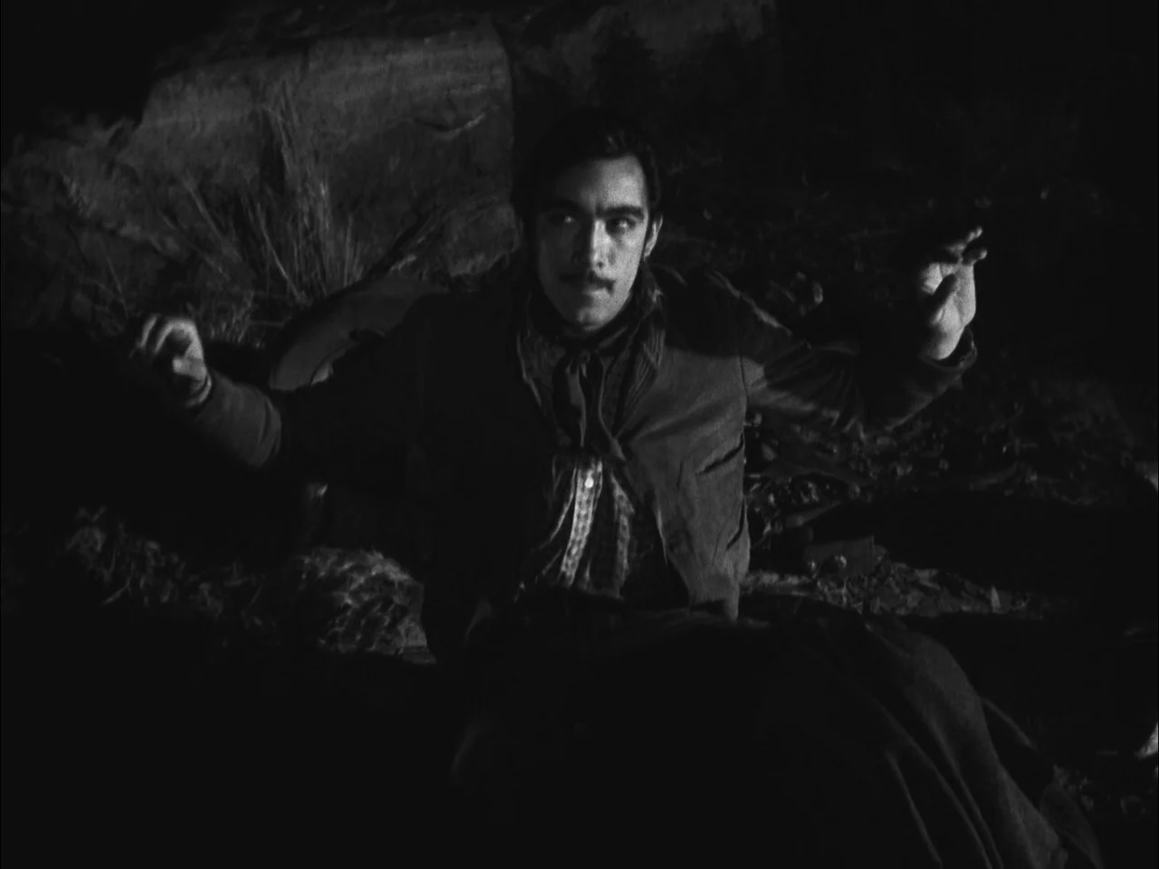 The Ox-Bow Incident (1942) movie still: medium — A dark, rocky landscape at night provides the backdrop for this outdoor scene. A young man with a…