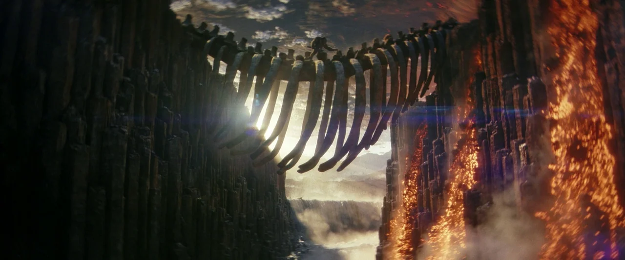 Godzilla x Kong: The New Empire (2024) movie still: wide — A colossal rib cage spans a deep gorge lined with vertical basalt columns. Molten lava…