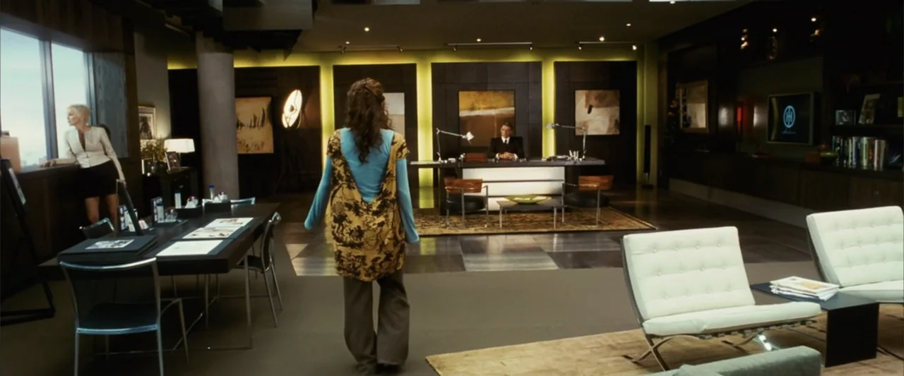 Catwoman (2004) movie still: wide — A modern, spacious executive office with dark paneled walls, a large desk, and large windows. A woman walks…
